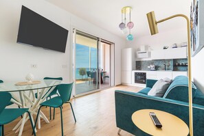 A modern living room with a glass dining table, teal chairs, a teal sofa, a TV mounted on the wall, and a kitchen area with a stove and cabinets. - Casa Sibiana by BarbarHouse (Gallipoli)