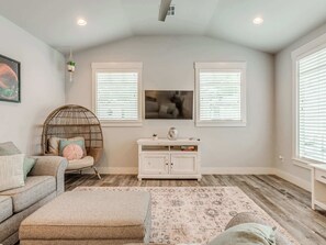 A living room with a sofa, a round wicker chair, a white cabinet, and a patterned rug.