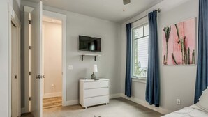 Un dormitorio con una cama, un aparador, un televisor y una ventana con cortinas.