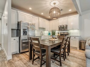 A modern kitchen with white cabinetry, stainless steel appliances, a wooden dining table, and a hanging light fixture. - Peace of Mind - Pet Friendly Luxury Getaway in Carlton Landing (Eufaula)