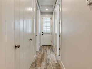 A hallway with white doors, a wooden floor, and a window with blinds. - Peace of Mind - Pet Friendly Luxury Getaway in Carlton Landing (Eufaula)