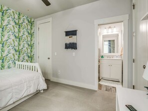 Une chambre à coucher comprenant un lit, une œuvre d’art accrochée au mur, une porte et une salle de bain avec un miroir et un lavabo.