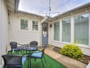Une terrasse avec une table et des chaises, une porte décorée d’une guirlande et un petit jardin.