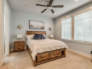 A bedroom with a bed, nightstands, a ceiling fan, a window with blinds, and a wall-mounted picture.