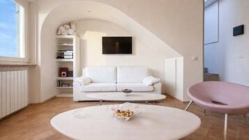 Un soggiorno moderno con un divano bianco, un tavolino rotondo, una poltrona rosa e una TV a parete.