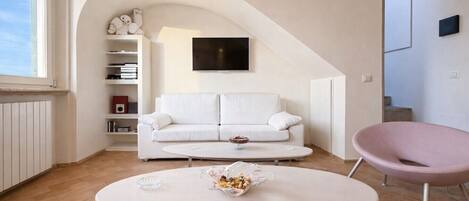 A modern living room with a white sofa, a round coffee table, a pink chair, and a TV mounted on the wall.