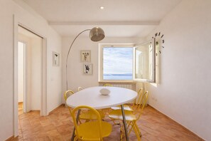 Un'area pranzo con un tavolo rotondo, sedie gialle, una tovaglia bianca e una lampada a sospensione.