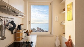 Une cuisine avec vue sur la mer, un poêle, des casseroles suspendues et un porte-serviettes.