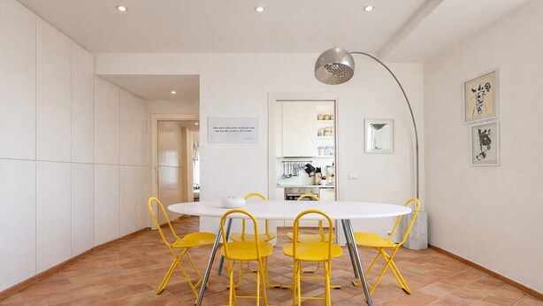 A dining area with a round table and yellow chairs, a kitchen in the background, and a modern pendant light. - Charming 2-Bedroom Home | Terrace & Great Lake View (Anguillara Sabazia)