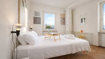 Een hotelkamer met een bed, nachtkastje, lamp, raam en kunstwerken aan de muur.