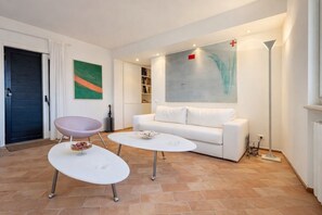 A modern living room with a white sofa, two white tables, a pink chair, and artwork on the walls.
