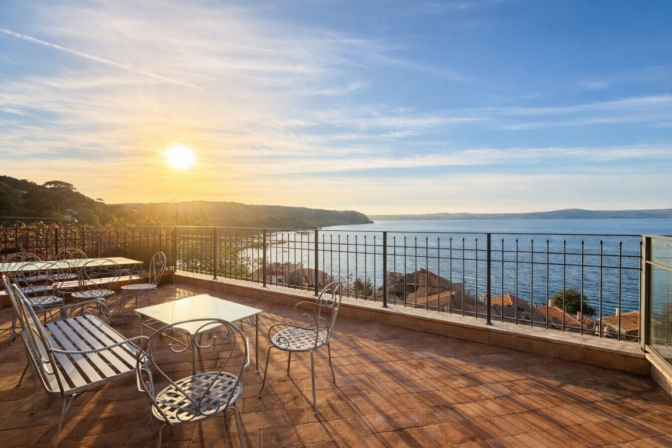 Una terrazza con tavoli e sedie, affacciata su uno specchio d'acqua e delle colline.
