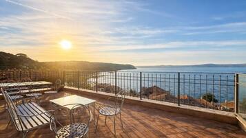 Una terrazza con tavoli e sedie, affacciata su uno specchio d'acqua e delle colline.