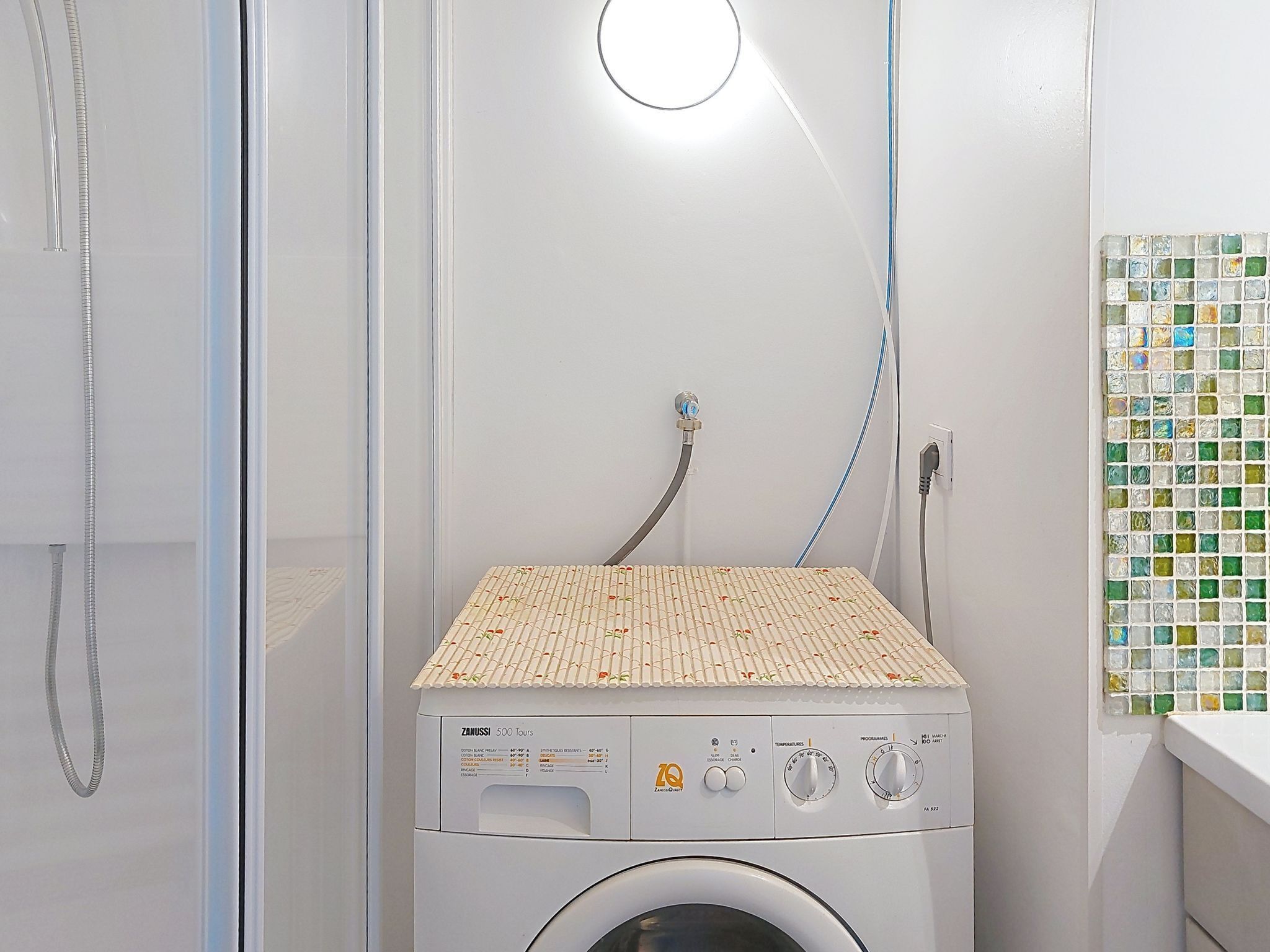 A front-loading washing machine with a control panel, a hose, and a tiled top.