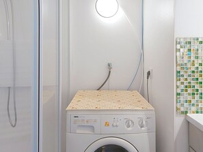 Eine Waschmaschine mit Frontlader, einer Bedienblende, einem Schlauch und einer gefliesten Oberseite.