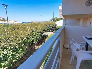 Ein Balkon mit Blick auf einen angelegten Garten, einem weißen Geländer und einem Tisch mit Stühlen.