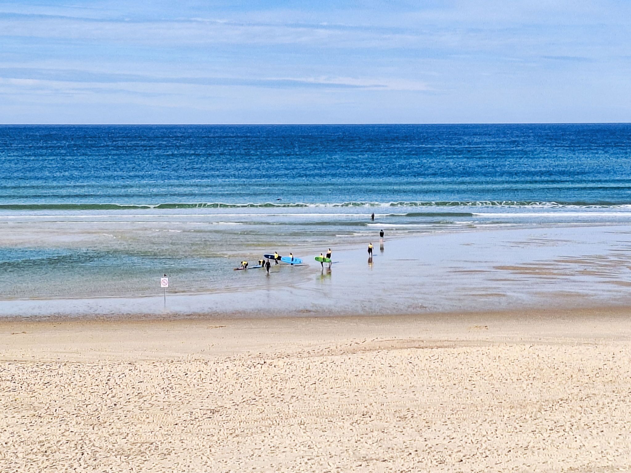 A beach with people walking and carrying surfboards.