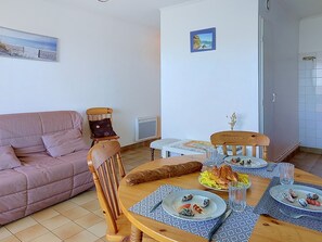 Ein Essbereich mit einem Tisch für zwei Personen, einem Holzstuhl, einer Couch und einem an der Wand befestigten Bild.