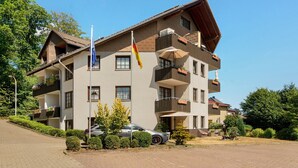 Un edificio a più piani con balconi, una bandiera e un'auto parcheggiata davanti.