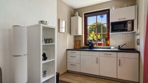 A compact kitchen with white cabinets, a microwave, and a window with a view of greenery outside. - Apartment 'Harzidyll' with Wi-Fi (Bad Sachsa)