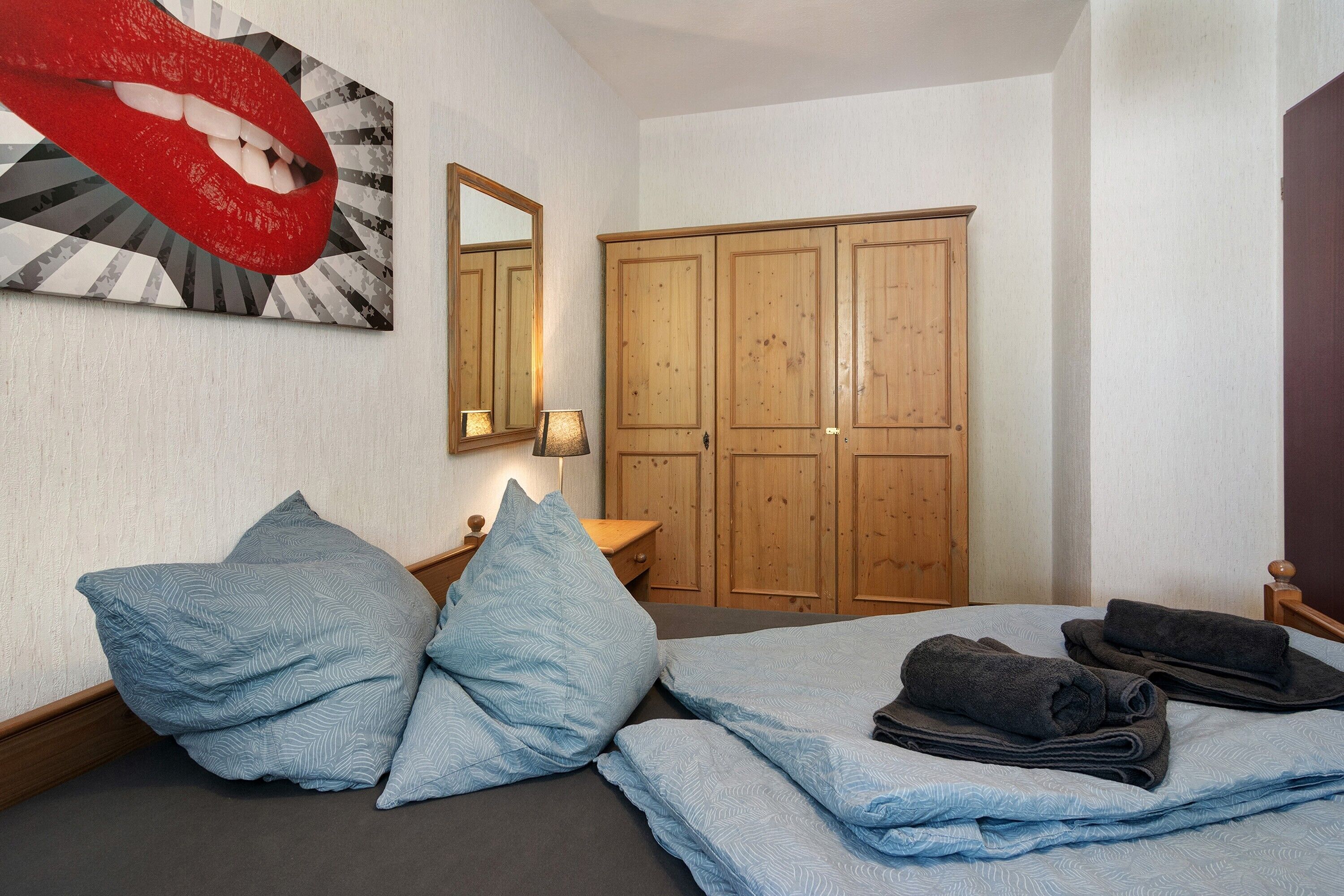 A bedroom with a bed, pillows, a mirror, a wardrobe, and a wall art piece.