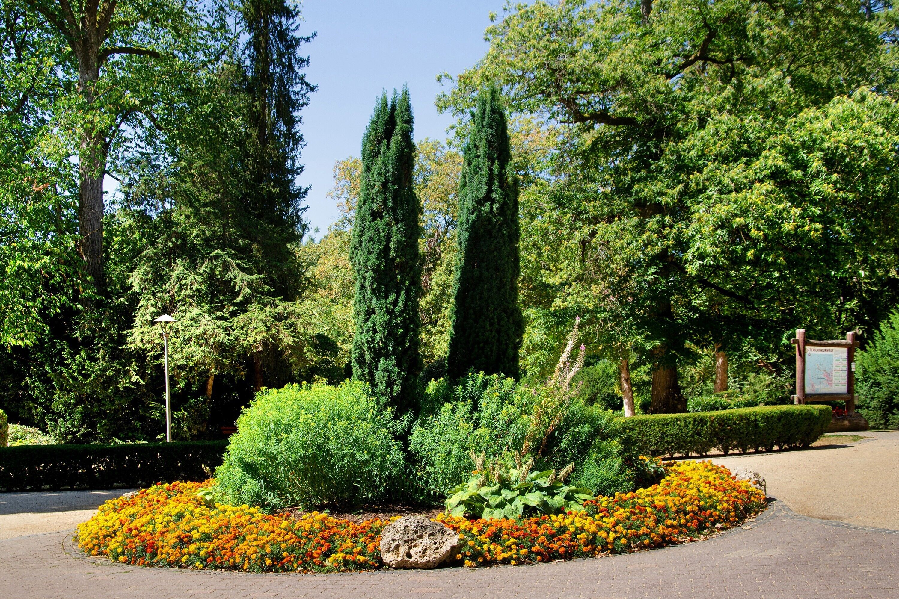 A landscaped garden with a variety of trees, a central bush, and a flower bed with orange and yellow flowers.