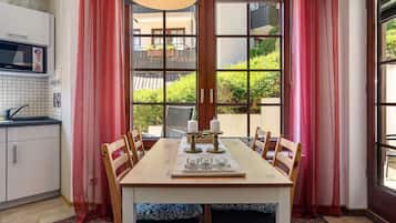 A dining area with a table set for six, a kitchen with white cabinets, and a view of greenery outside.