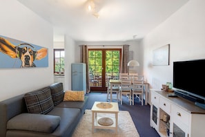 Een woonkamer met een bank, een salontafel, een televisie en een eethoek met stoelen en een tafel.