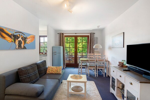 Ein Wohnzimmer mit einer Couch, einem Couchtisch, einem Fernseher und einem Essbereich mit Stühlen und einem Tisch.