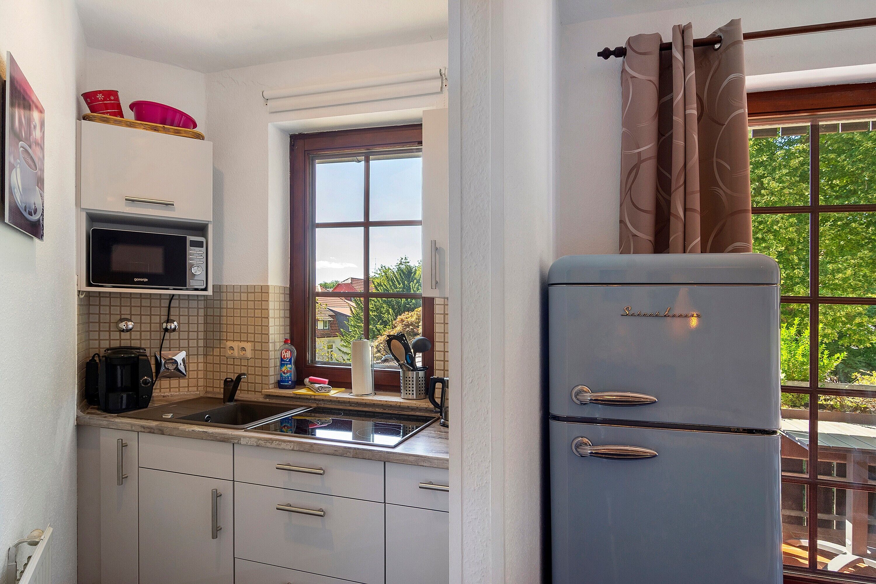 A kitchen with a built-in microwave, a refrigerator, and a window with a view of greenery.