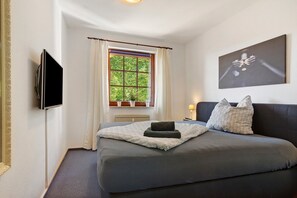 Een slaapkamer met een bed, een aan de muur bevestigde televisie, een raam met gordijnen en een schilderij.