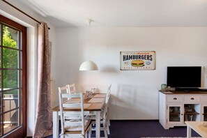 Een kamer met een eettafel, stoelen, een televisie en een bord dat hamburgers aanprijst.