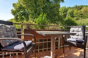 Eine Terrasse mit Korbmöbeln und einem Tisch, umgeben von einem Holzzaun und Bäumen.