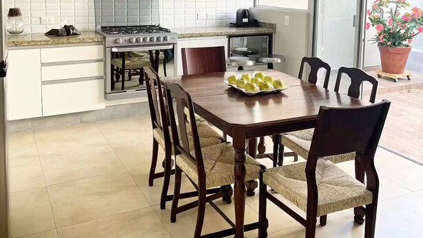 A modern kitchen with white cabinetry, a dining table with chairs, a stove, and a large window with a view. - Piece Of Paradise In The City (Guadalajara)