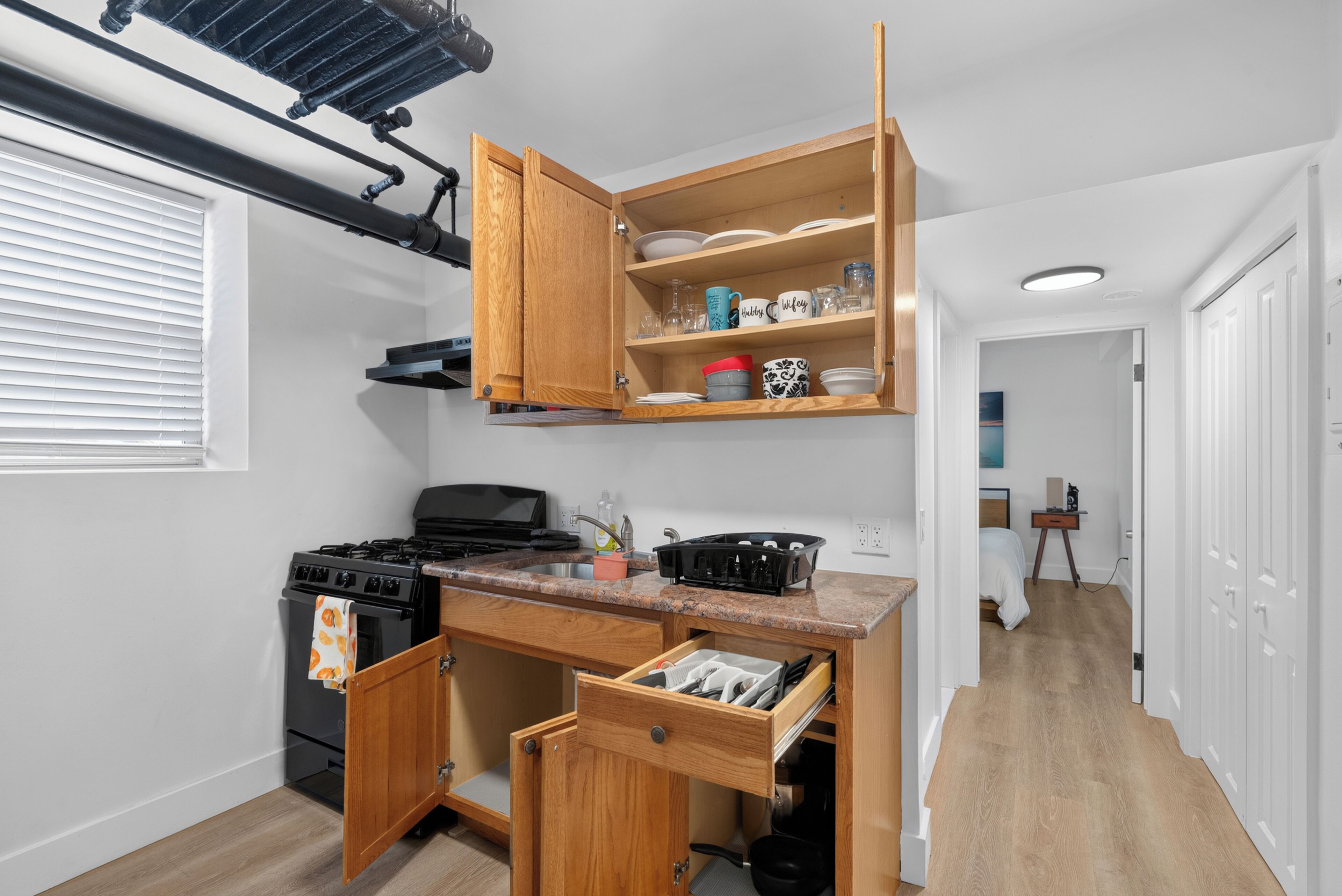 Una cocina compacta con estufa a gas, armarios de madera y encimera con escurreplatos.
