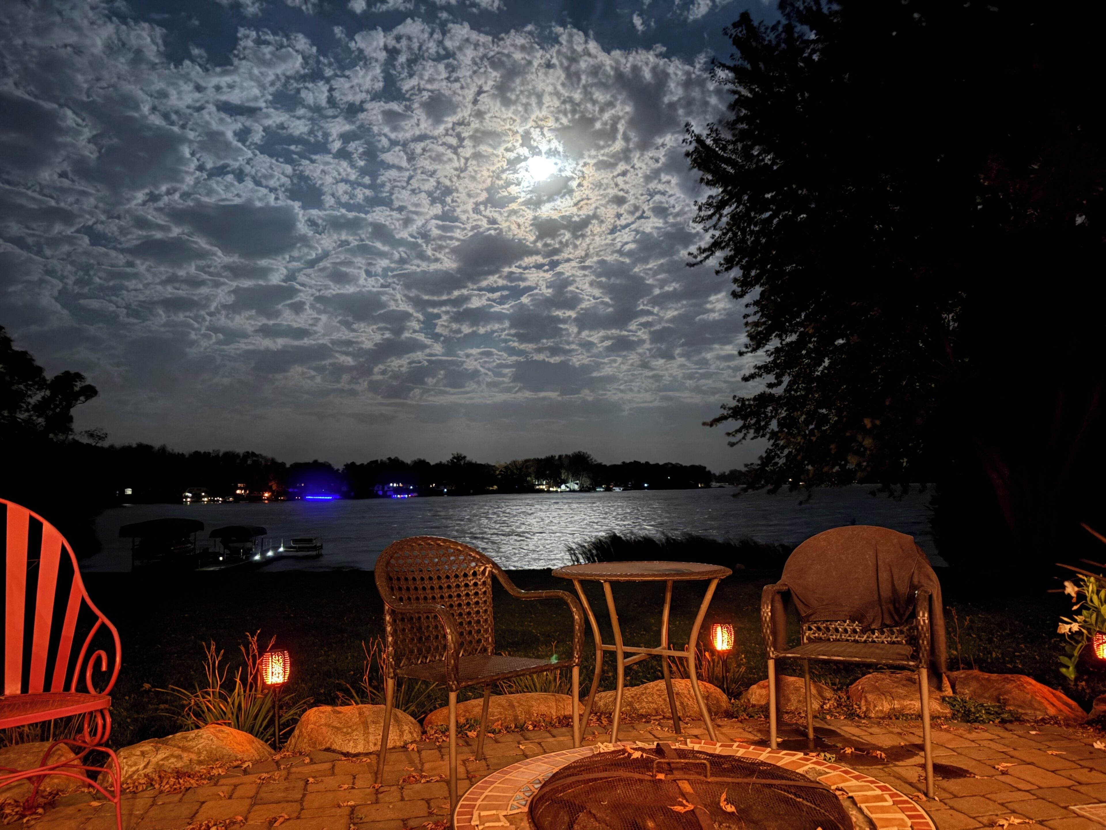 Un espace extérieur aménagé avec des chaises et une table, offrant une vue sur une étendue d’eau, le ciel et les nuages.