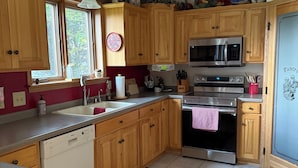 Una cocina con armarios de madera, horno de acero inoxidable, microondas y lavavajillas.
