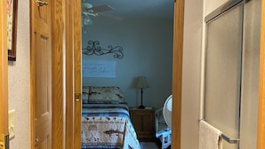Un pasillo que conduce a un dormitorio con una cama, una mesita de noche, una lámpara y un cartel decorativo en la pared.