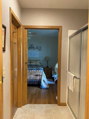 Ein Flur, der in ein Schlafzimmer mit einem Bett, einem Nachttisch, einer Lampe und einem dekorativen Wandschild führt.