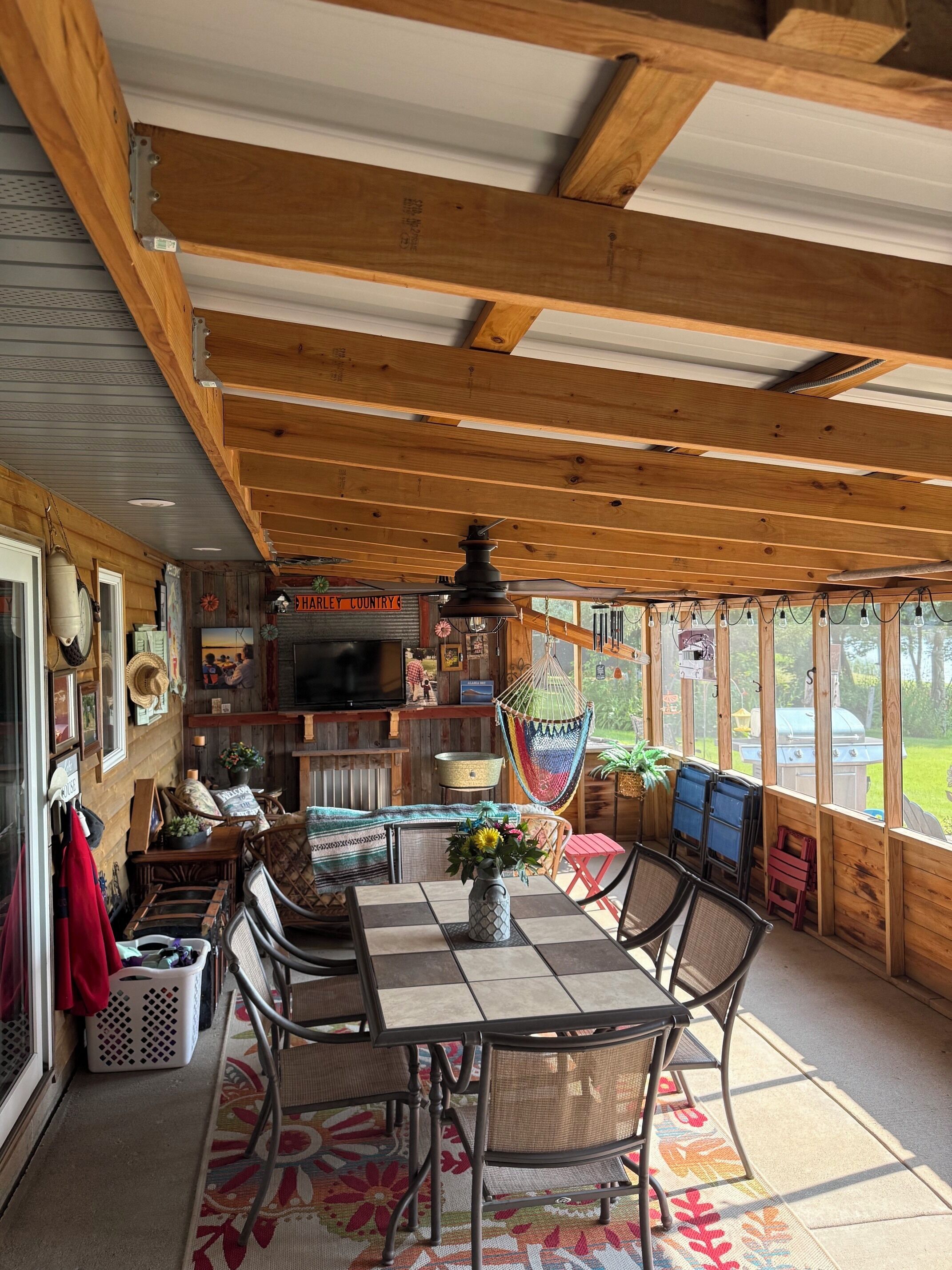 A covered outdoor dining area with a table and chairs, a hanging hammock, and a view of the outdoors.