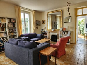 A living room with a sofa, armchair, coffee table, and fireplace. There are bookshelves and a large mirror.