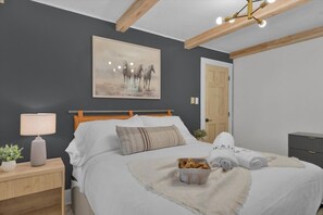 Quarto com cama, mesa de cabeceira, abajur e um quadro na parede.