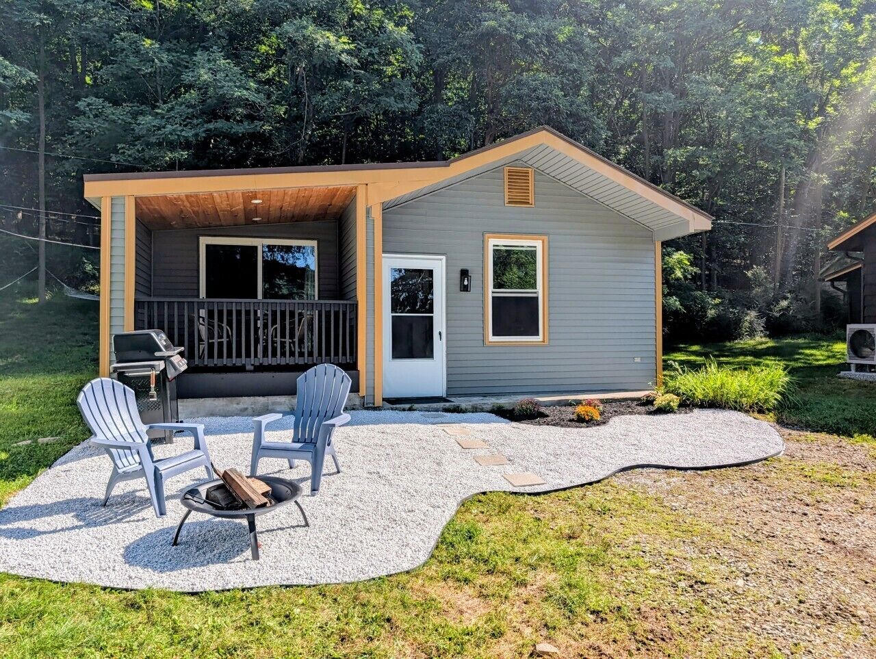 A small house with a covered patio, two Adirondack chairs, a grill, and a fire pit.