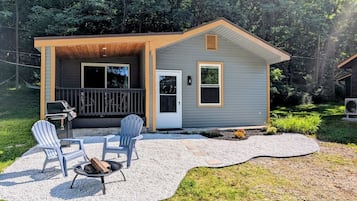 A small house with a covered patio, two Adirondack chairs, a grill, and a fire pit.