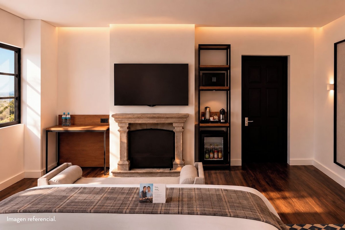 A bedroom with a bed, a fireplace, a TV mounted above it, and a door leading to another room.