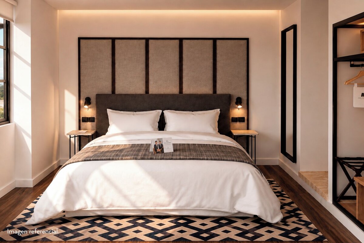 A hotel room with a large bed, bedside lamps, a headboard, a wooden floor, and a wardrobe with a mirror.