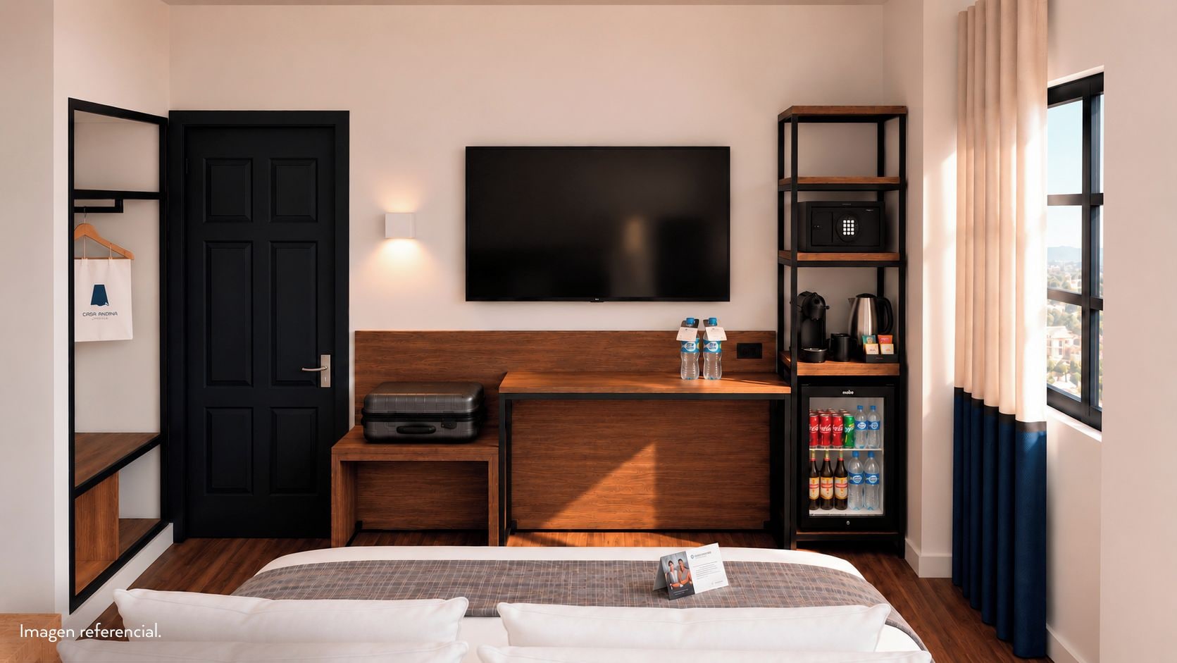 Quarto de hotel com cama, televisão de tela plana na parede, minibar, cabideiro e janela com cortinas.