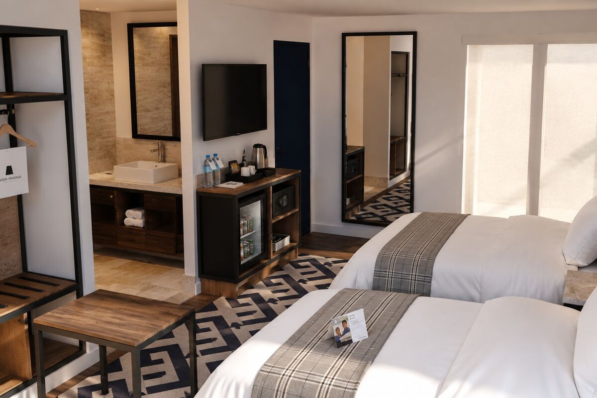 A hotel room with two beds, a desk, a vanity, a television, and a large mirror.