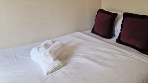 A neatly made bed with white linens and two dark pillows, a wall-mounted artwork above it, and a plain wall. - A Room Double bed 2 People With Hob and Fridge (London)