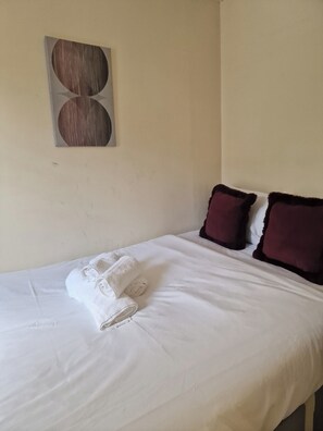 Ein ordentlich bezogenes Bett mit weißen Laken und zwei dunklen Kissen, ein Wandbild darüber und eine schlichte Wand.